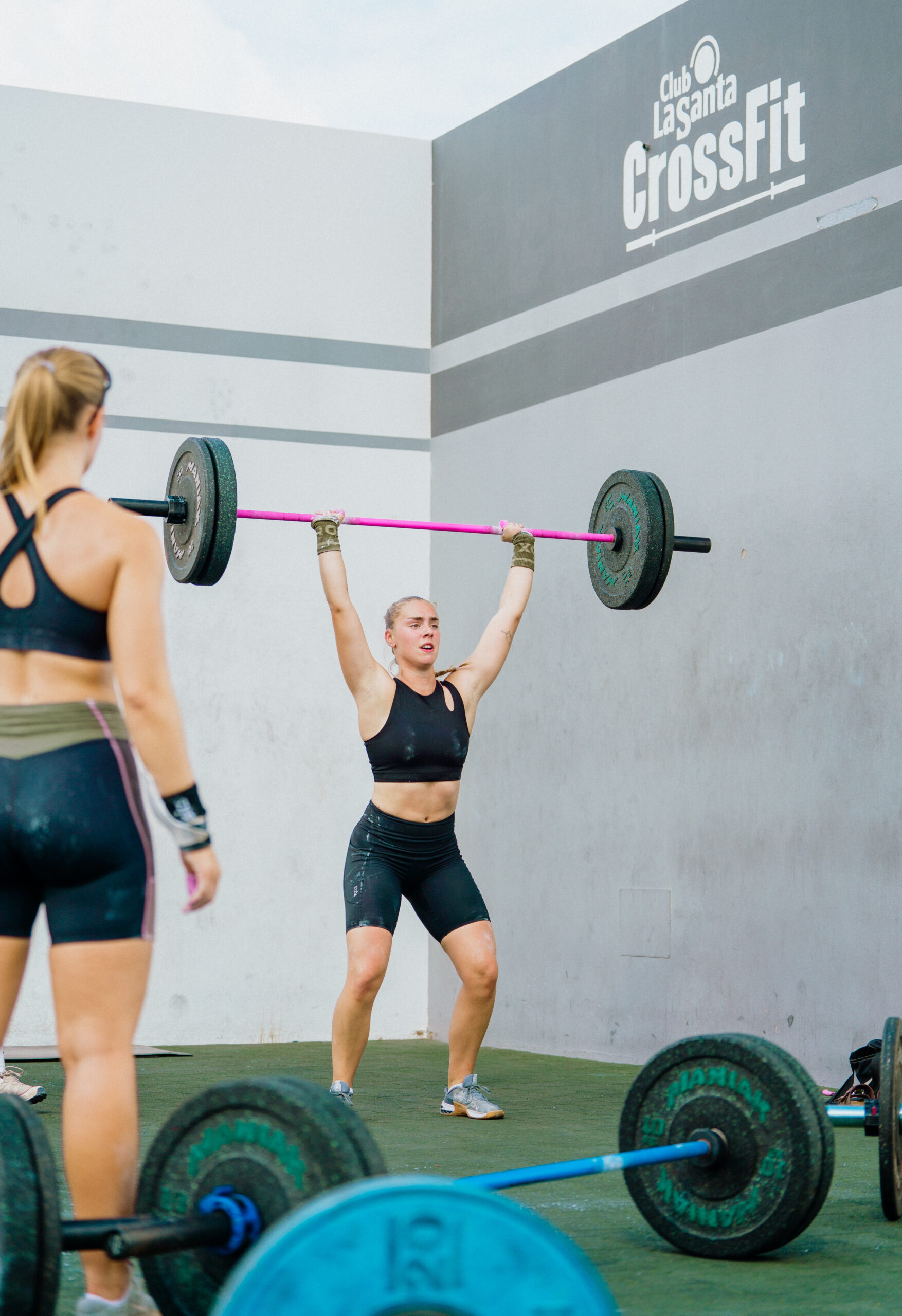 A blonde woman lifting a heavy bar above her head in a power and strength class at Club La Santa.