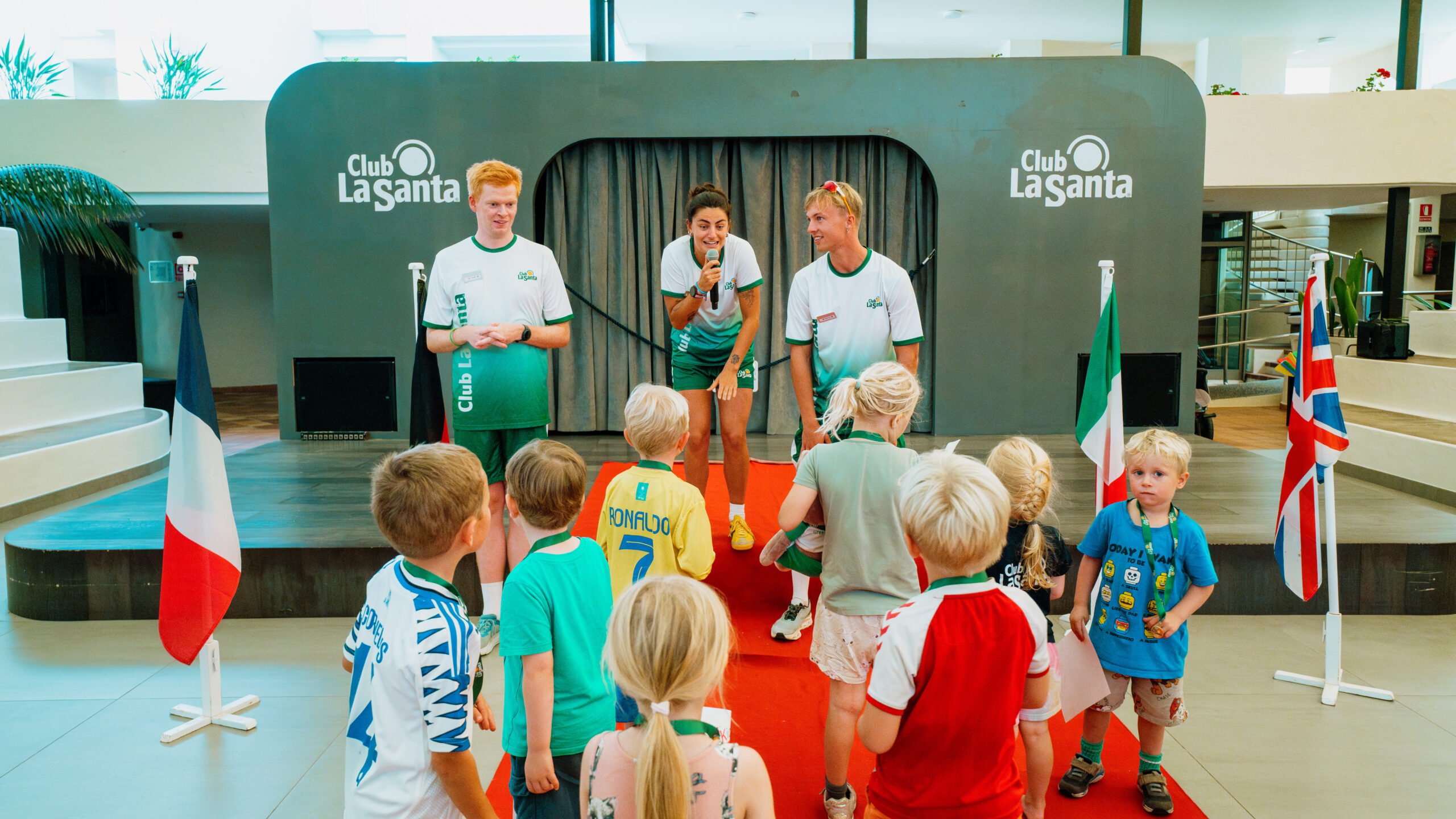3 kids club staff talking to a group of children from the stage
