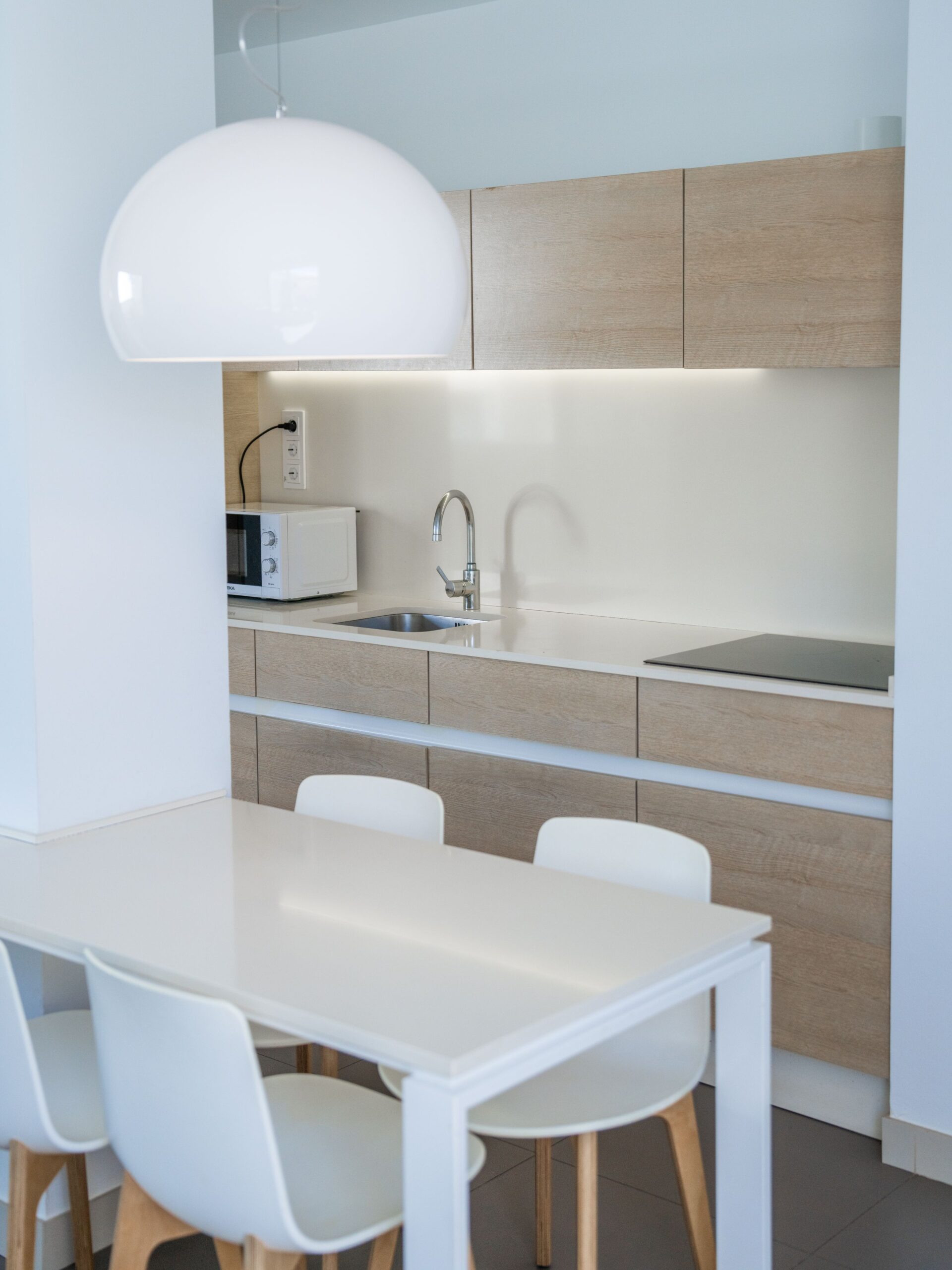 A white dining table with 4 chairs, in front of the light wood kitchen cabinets.