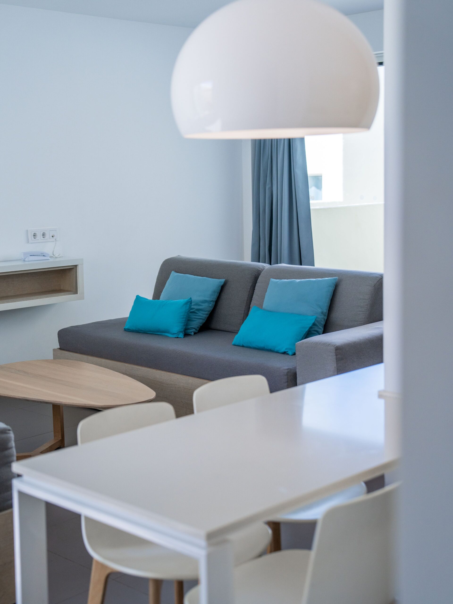 A kitchen living room, with a grey sofa bed with blue pillows in front of the glass patio door.