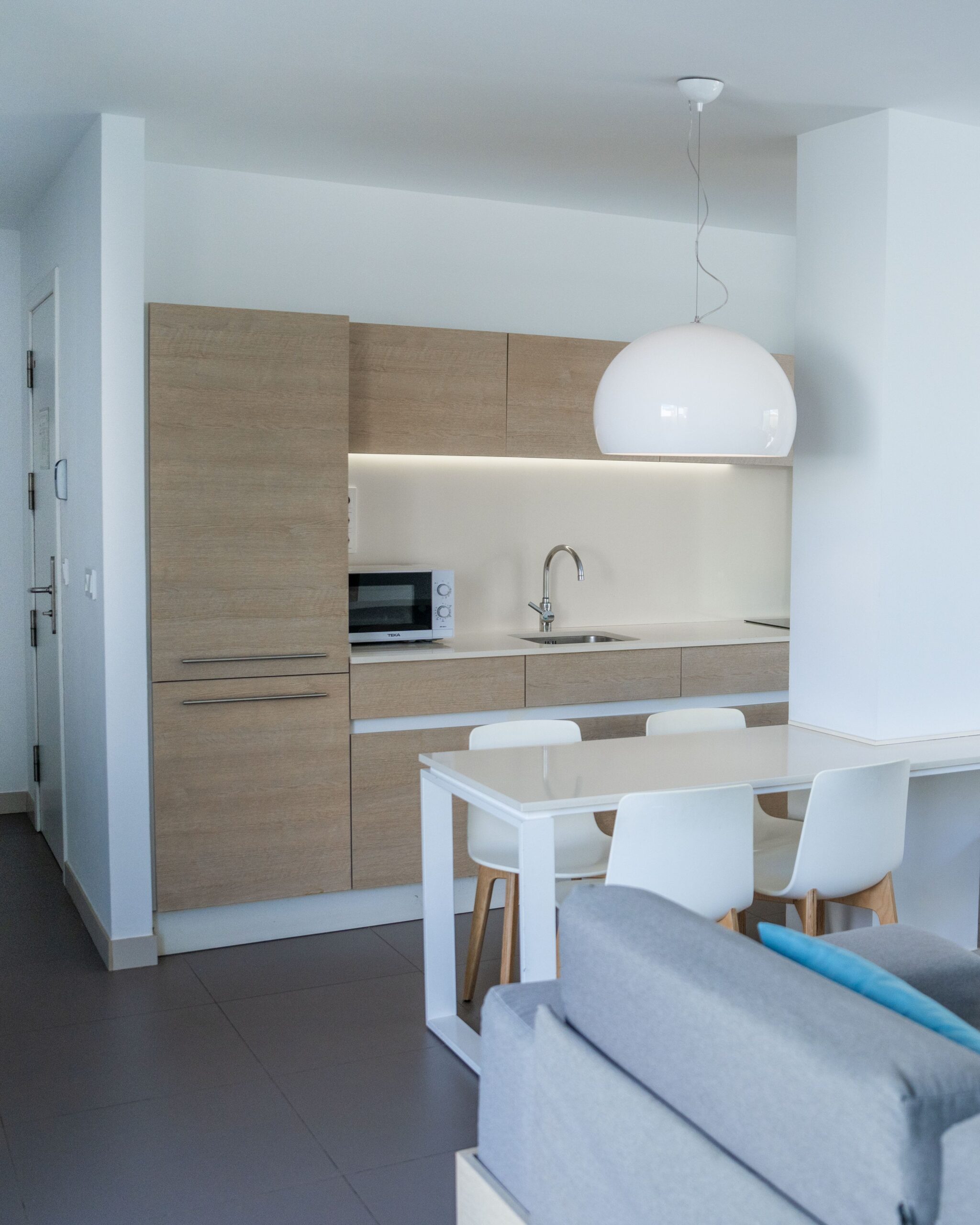 A white dining table with 4 chairs, in front of the light wood kitchen cabinets.