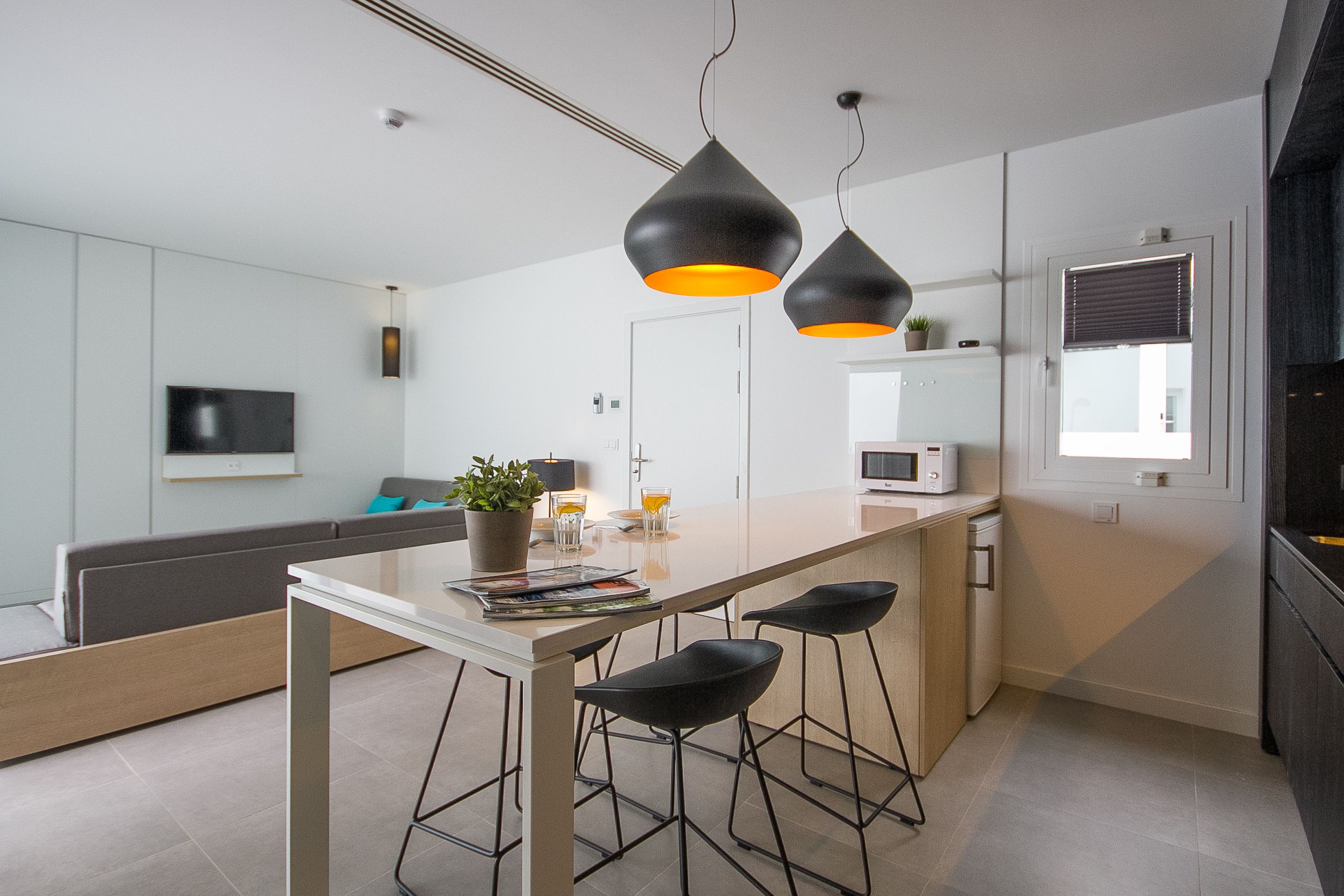 The kitchen/living room of a suite, with a corner sofa and TV, breakfast bar and black kitchen cabinets.