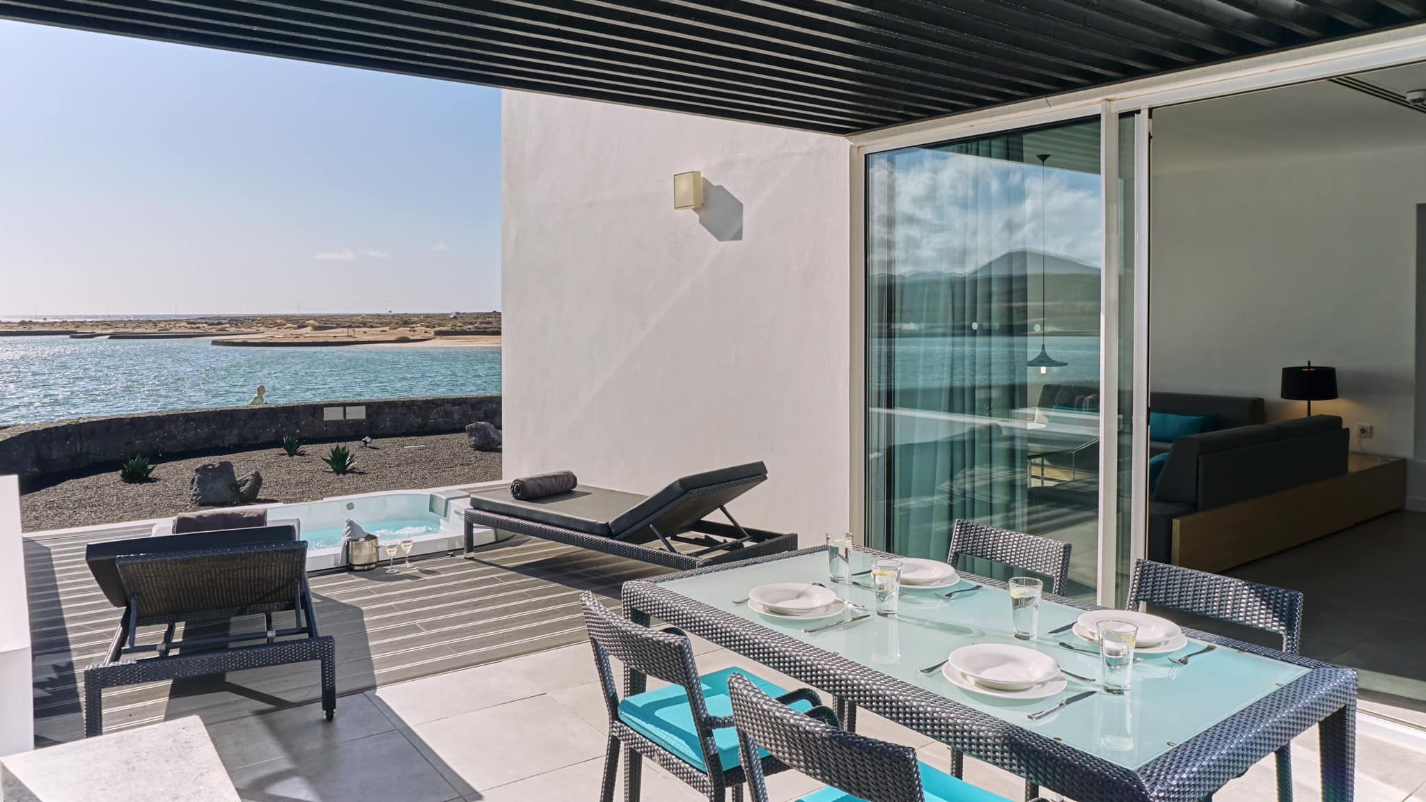 The terrace of the luxury suite, with 2 sunlounges, a laid dining table and a hot tub. There is a view of the sea.