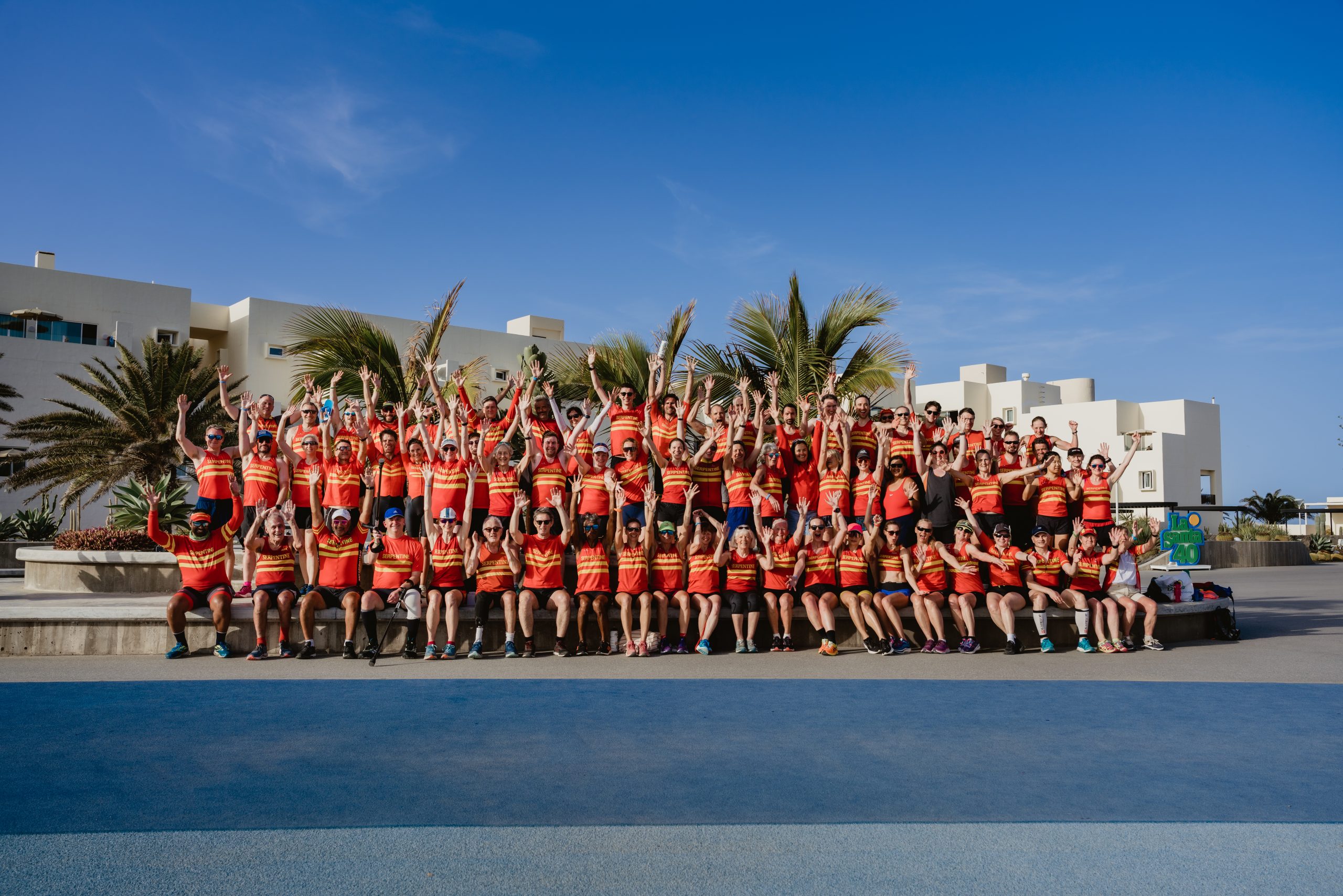 A large sports team, all wearing matching red sports uniform , having a group photo outside on the steps at Club La Santa
