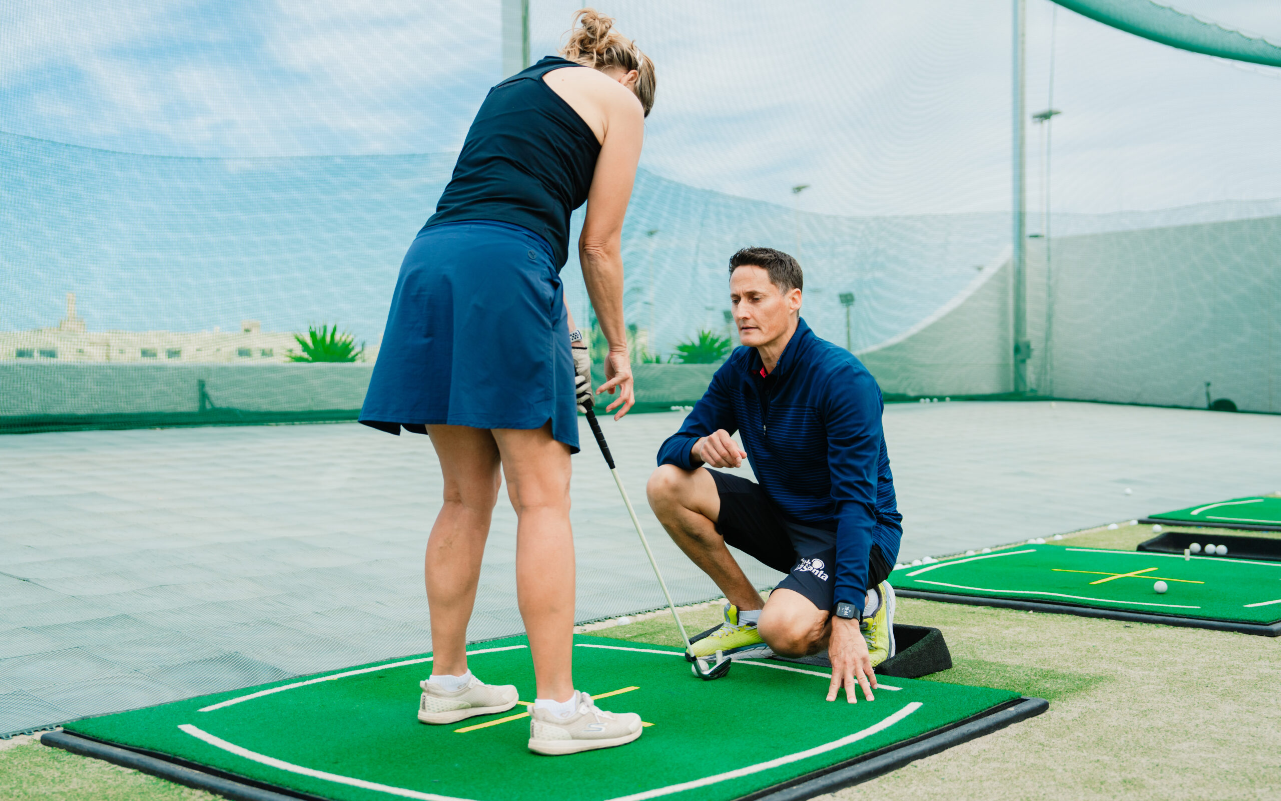 A woman holding a golf club at the driving range at Club La Santa. She is being guided by a male instructor.