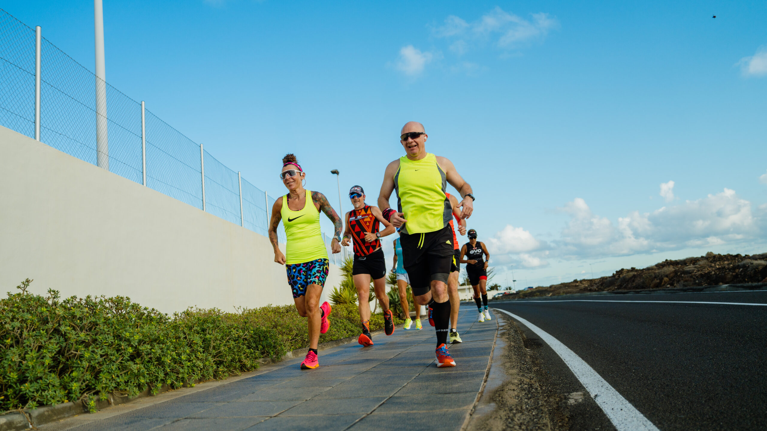 A group of adults wearing bright running gear, running together on the roads surrounding Club La Santa.