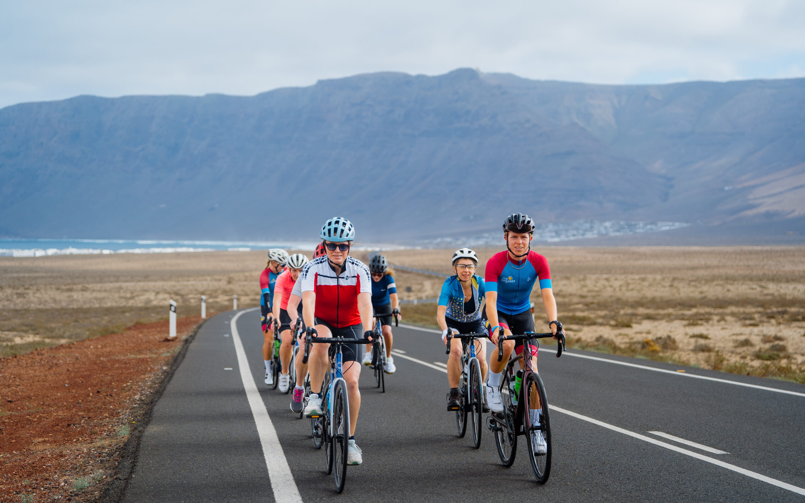 A group of women cycling in brightly colourd tri-suits through the mountainous terrain of Lanzarote.