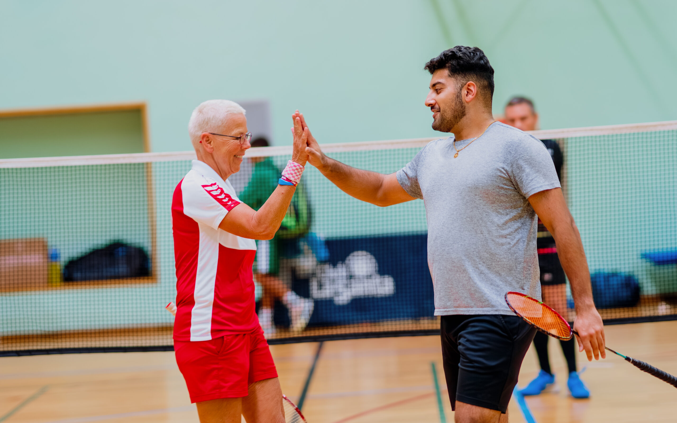 Two participants of a badminton tournamnet stood on the badminton court, high-fiving after a match.