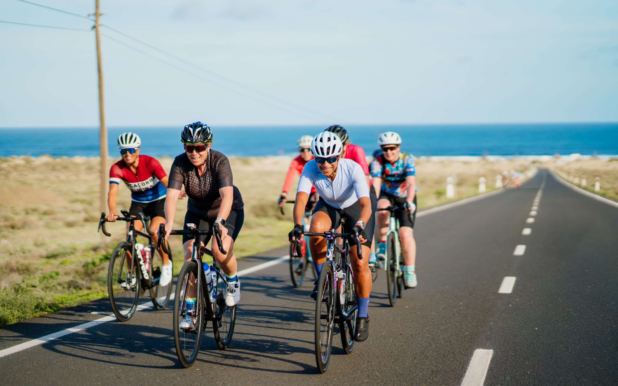 A group of tri-athletes cycling on the road, with rocky terrain in the background in Lanzarote.