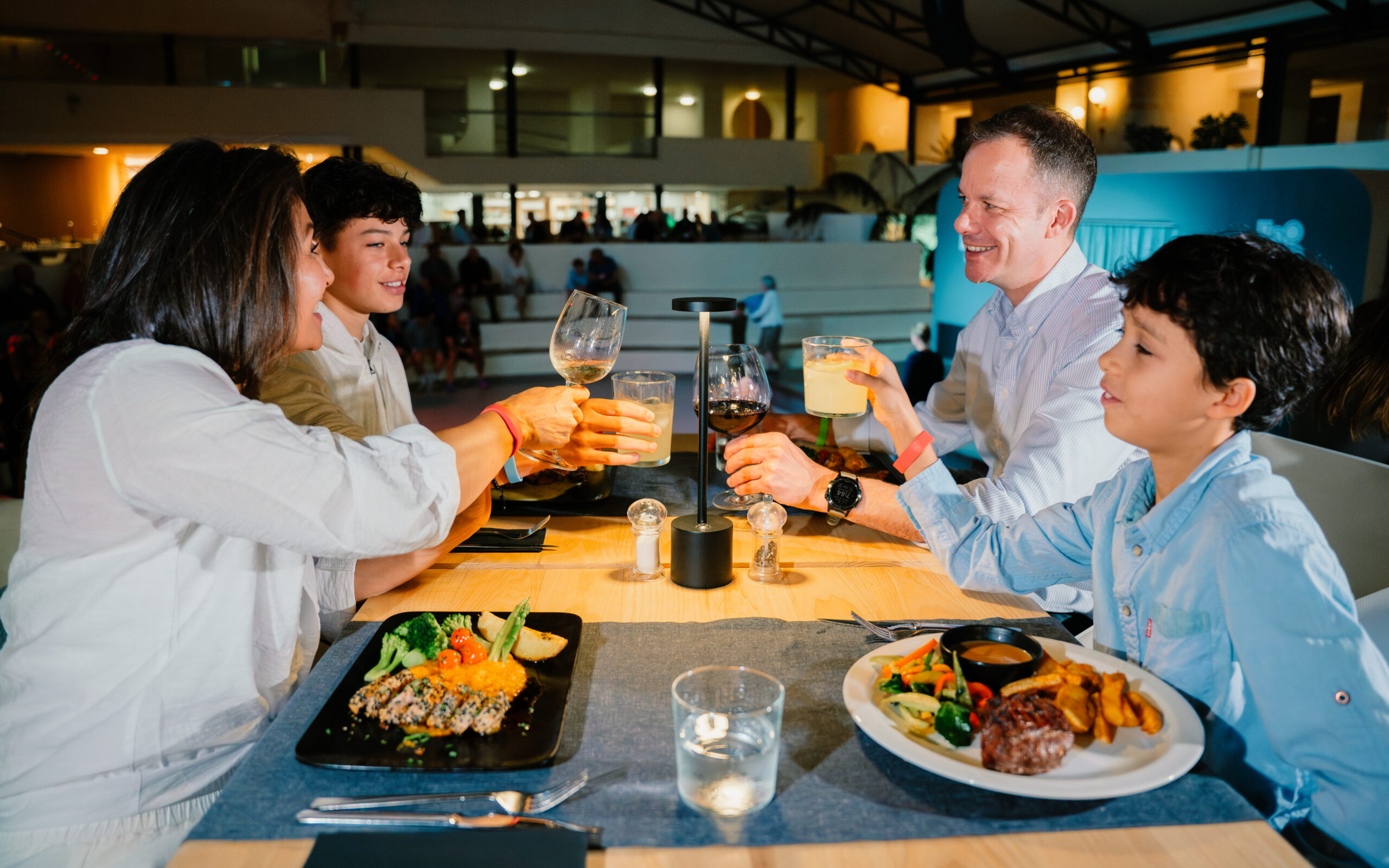 A family of four, sat eating food and drinking wine or juice in La Plaza restaurant at Club La Santa.