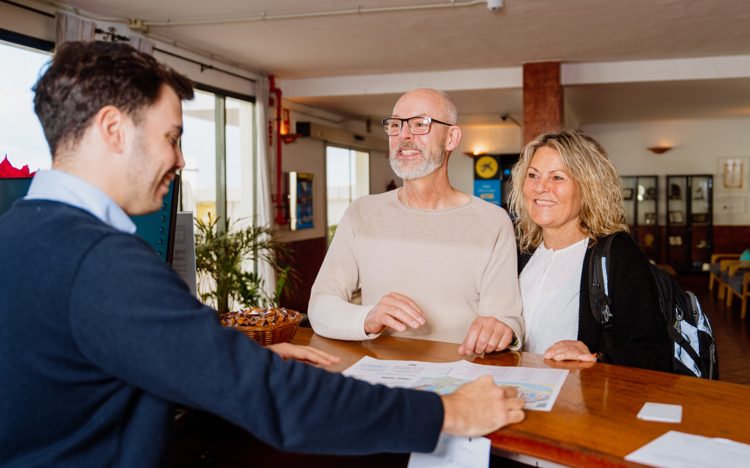 A couple smiling as they are shown information by the male receptionist at the check in desk.