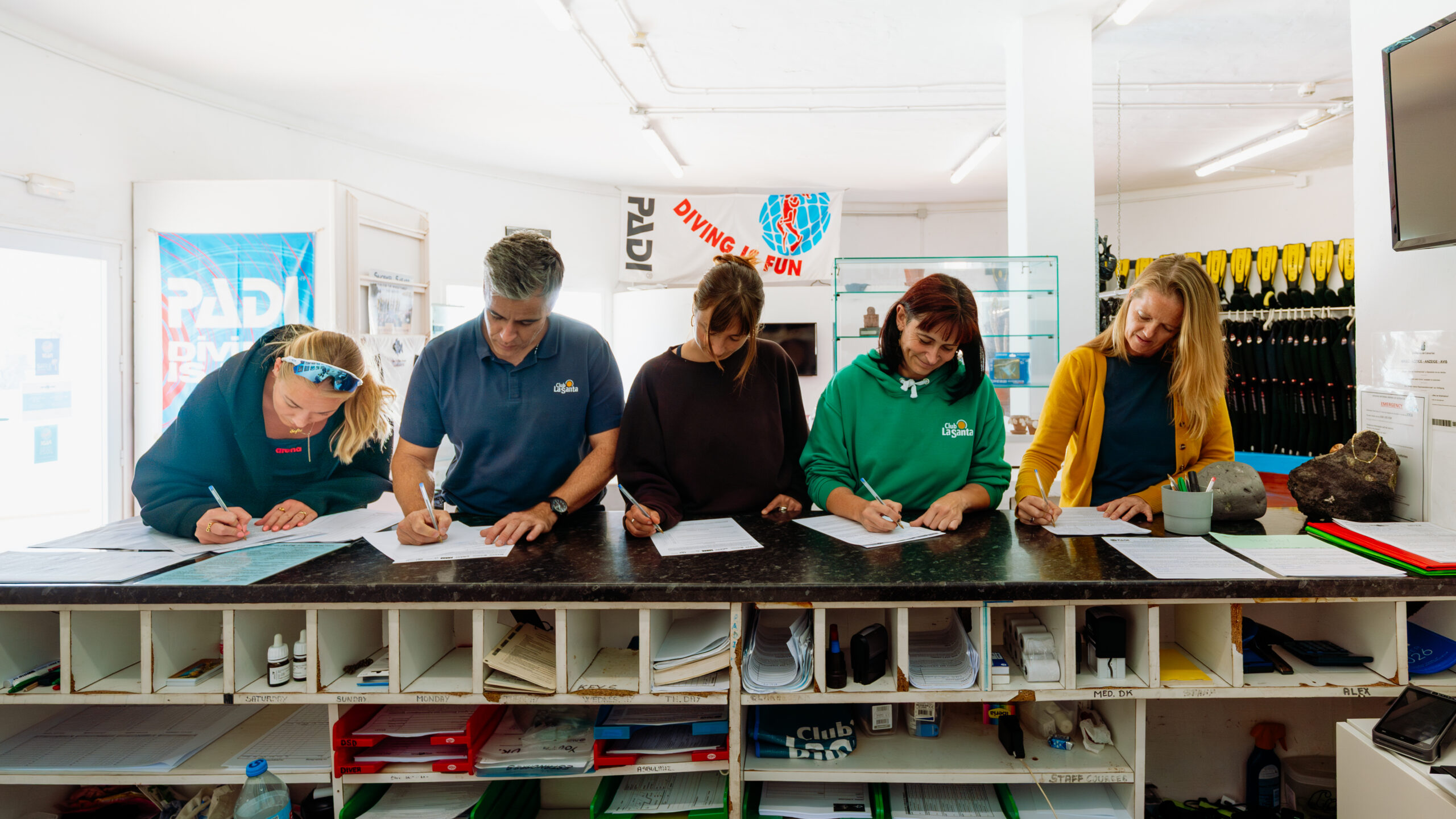 Five adults stood signing documents at the reception desk in the Dive Centre at Club La Santa.