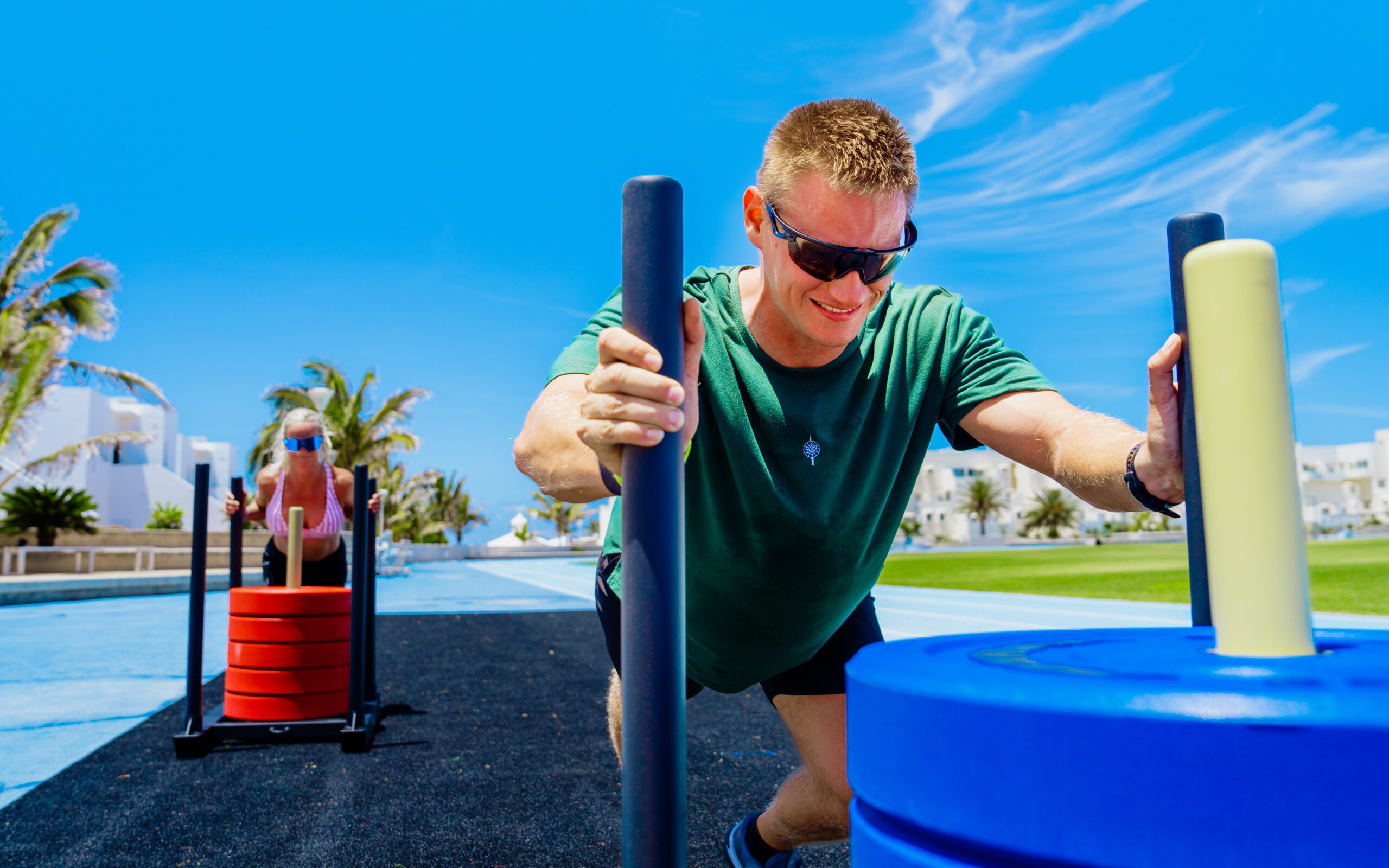 A man and a woman pushing sleds that are loaded with weighted plates in the functional area at Club La Santa