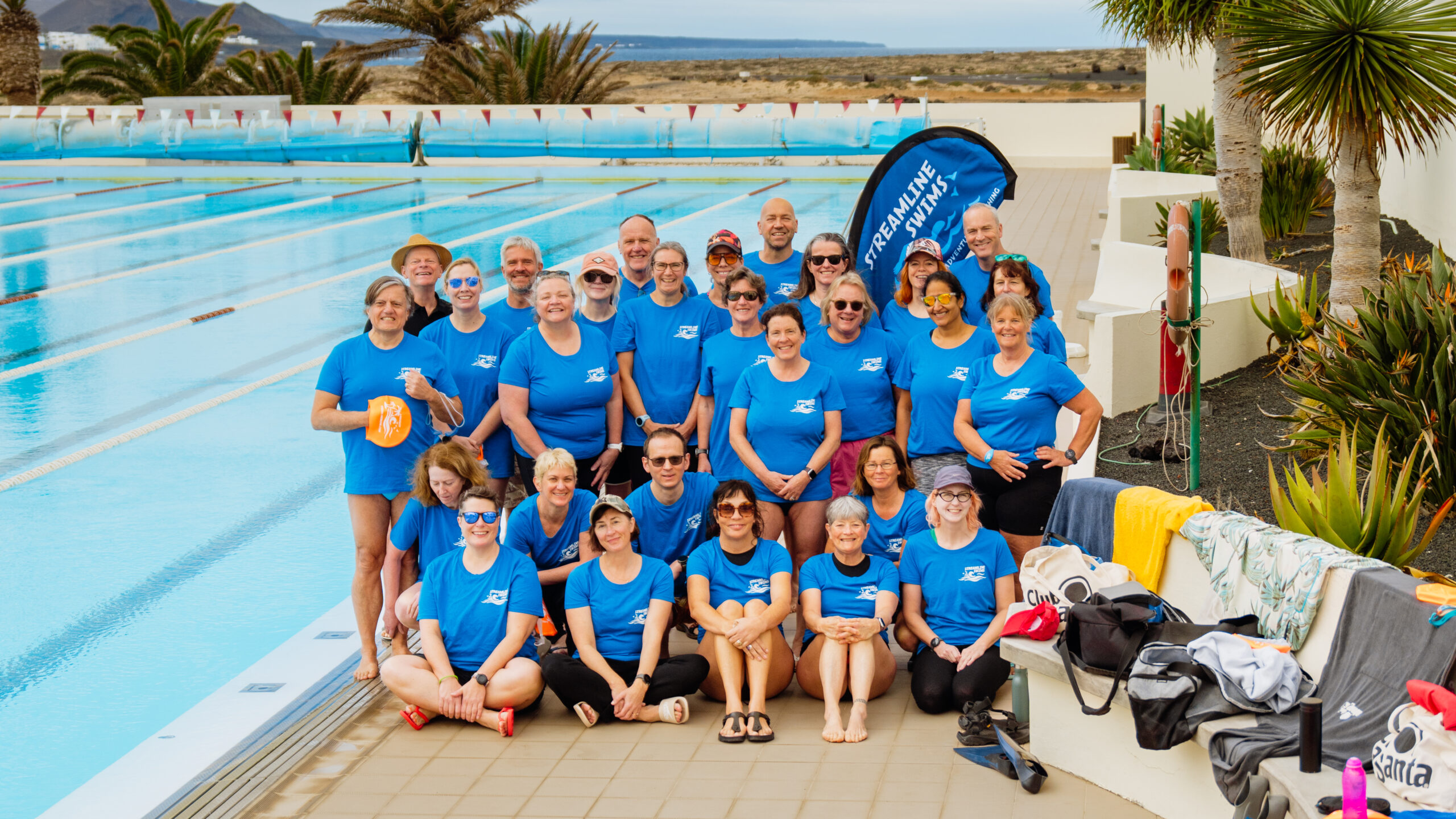 A group photo of Streamline Swim Club, stood by the 50m swimming pool at Club La Santa. They are all wearing matching blue t-shirts.